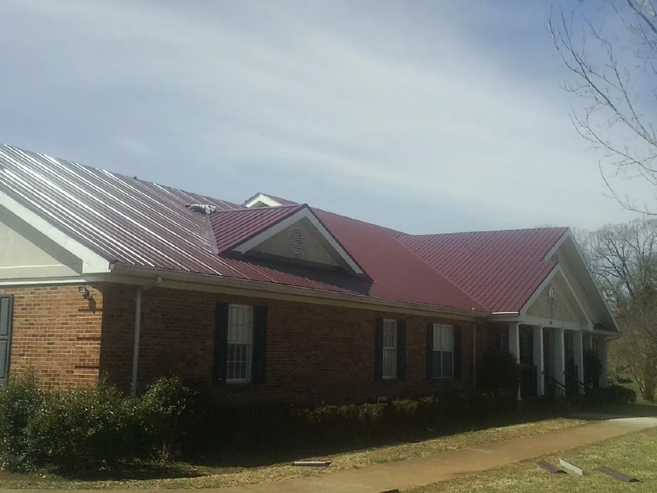 Red metal roof with gabled entries on a long brick building, from a Hail Damage Roof Repair job in Hillsboro